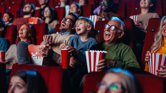 Spotlight on Father, daughter and grandfather laughing whilst watching a movie at the cinema eating popcorn. 